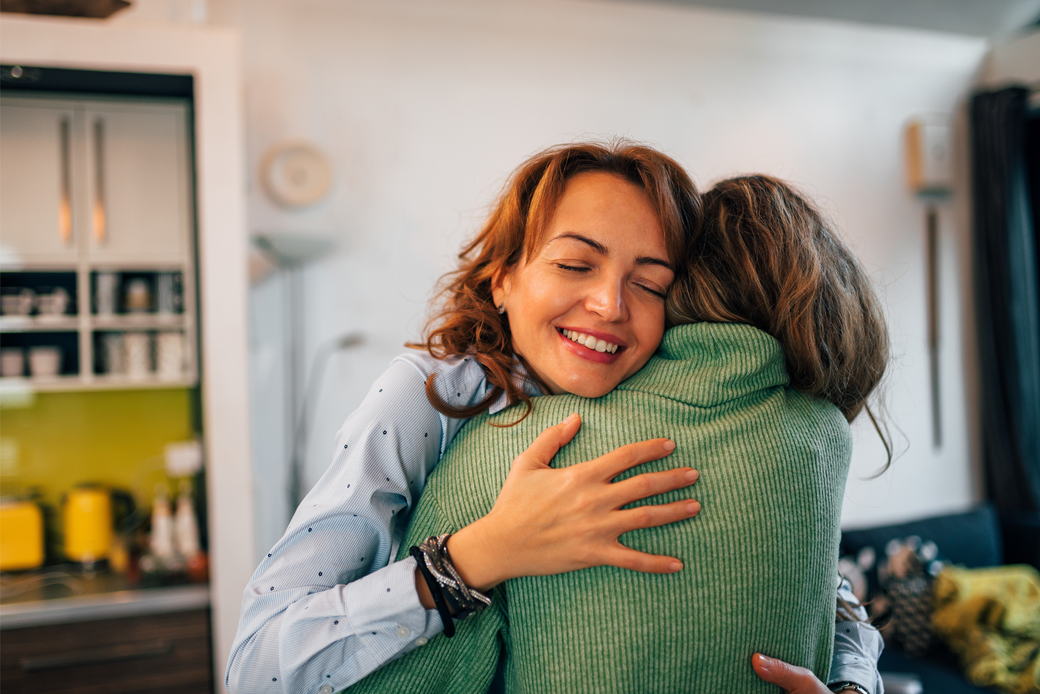 Two friends hugging for 20 seconds at home, smiling with eyes closed — the science-backed benefits of hugging